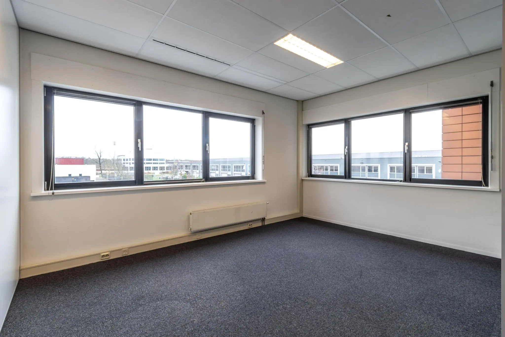 Lichte, lege kantoorruimte aan de Lage Biezenweg met grote ramen en blauw tapijt.